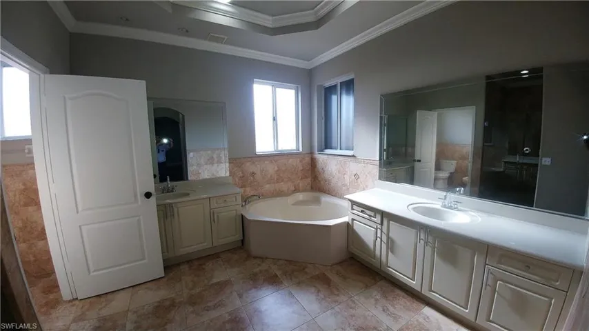 Features dual vanities & sinks, a large shower stall, a soaking tub, crown molding, and tile walls