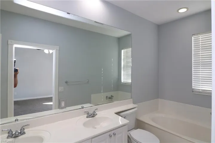 Bathroom featuring dual bowl vanity, toilet, and a bath to relax in