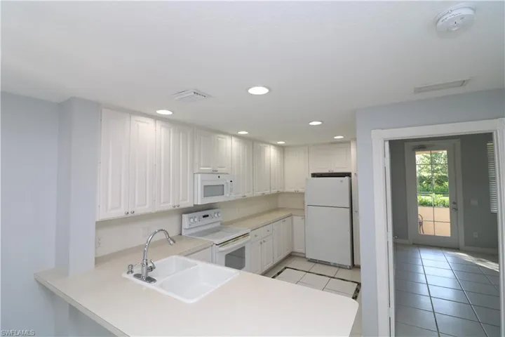 Kitchen with kitchen peninsula, white appliances, light tile flooring, sink, and white cabinets