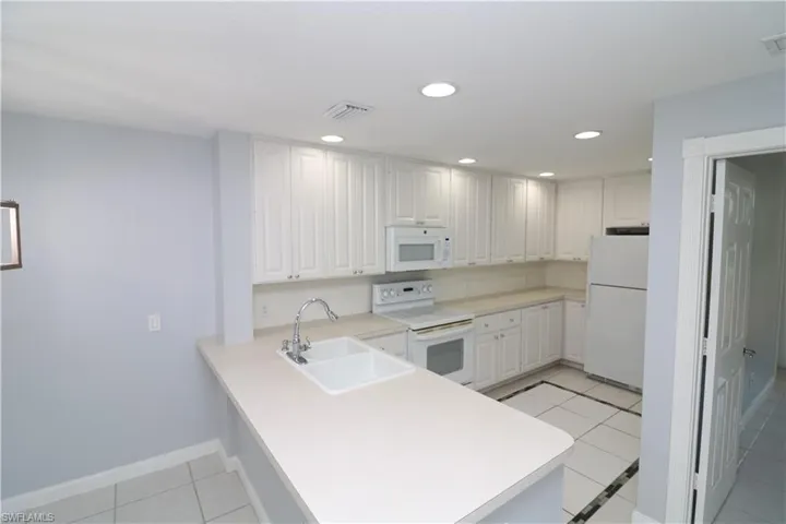 Kitchen featuring sink, white appliances, light tile floors, and kitchen peninsula
