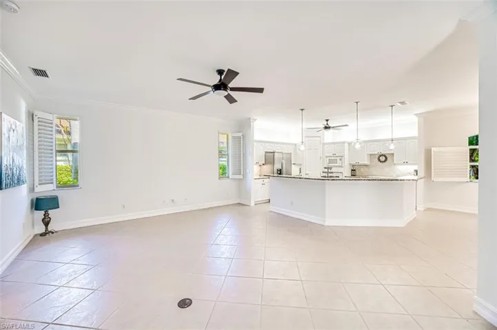 Unfurnished living room with ceiling fan, light tile patterned floors, crown molding, and a wealth of natural light