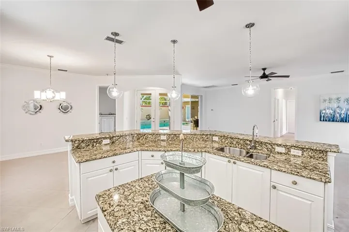 Kitchen with white cabinetry, sink, hanging light fixtures, a kitchen island with sink, and ceiling fan with notable chandelier