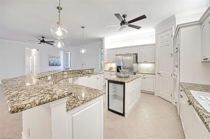 Kitchen featuring white appliances, pendant lighting, white cabinets, wine cooler, and a large island