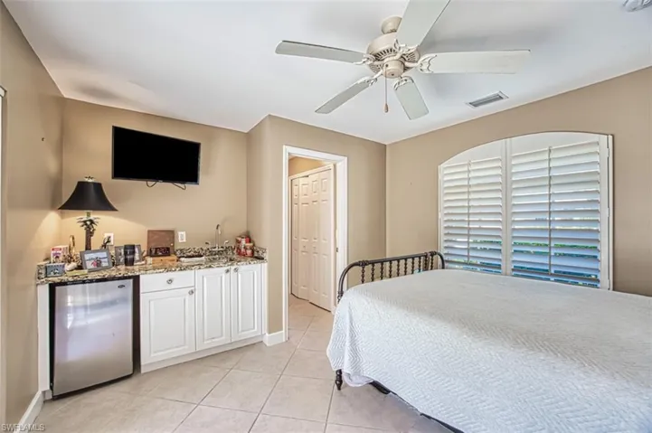 Bedroom featuring sink, ceiling fan, stainless steel fridge, light tile patterned floors, and a closet