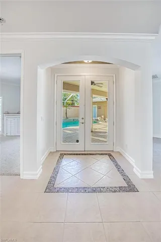 Doorway with french doors, light tile patterned floors, and ornamental molding