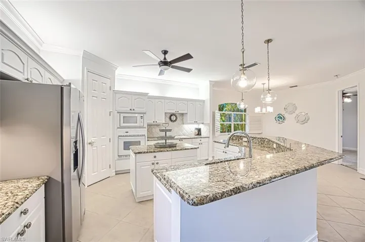 Kitchen with a kitchen island with sink, ceiling fan, hanging light fixtures, and white appliances