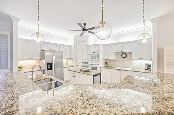 Kitchen featuring decorative backsplash, white cabinetry, hanging light fixtures, and white appliances