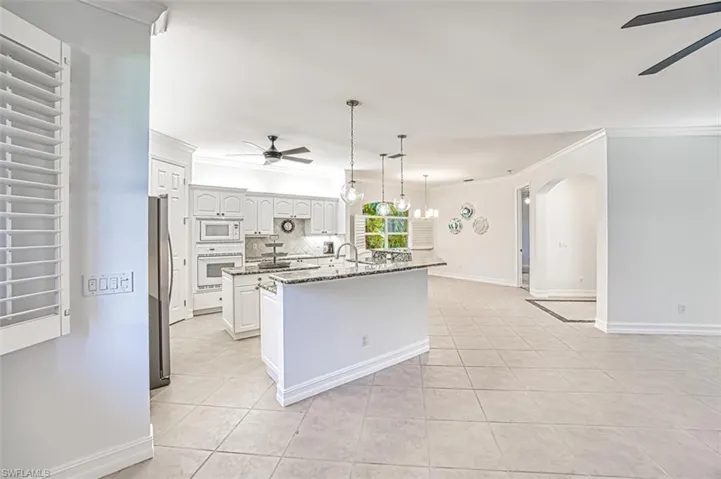 Kitchen with white appliances, stone counters, white cabinets, an island with sink, and light tile patterned flooring
