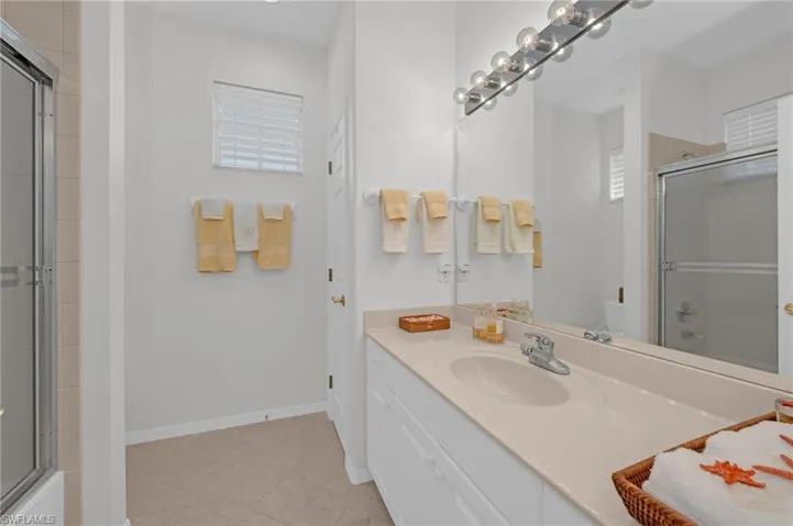 Bathroom with vanity, bath / shower combo with glass door, and light tile patterned floors