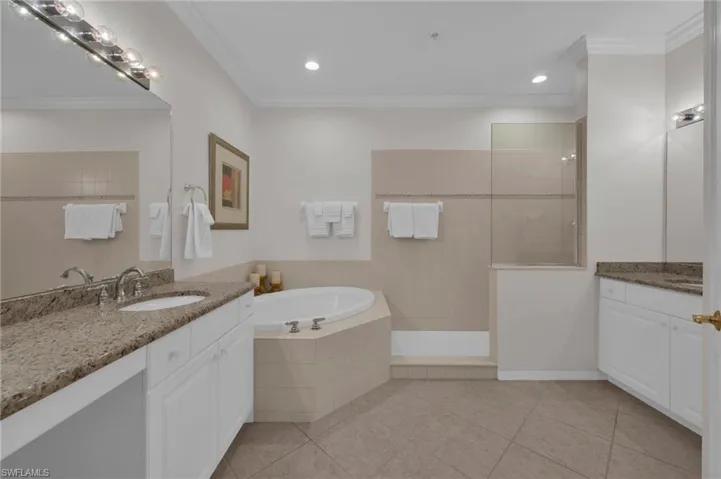 Full bath with two vanities, crown molding, a garden tub, light tile patterned floors, and a walk in shower