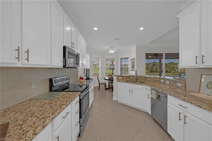 Kitchen featuring tasteful backsplash, appliances with stainless steel finishes, white cabinets, light stone countertops, and recessed lighting