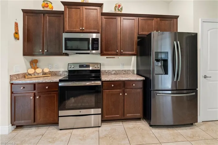 Kitchen with stainless steel appliances, dark brown cabinets, and light stone counters