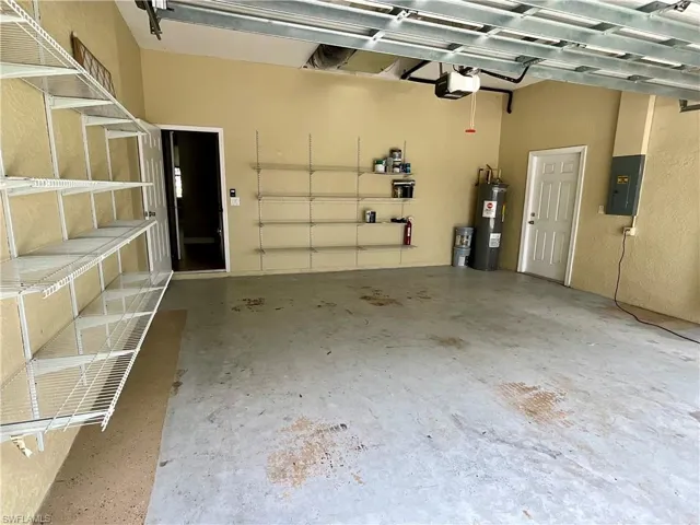 Garage featuring electric panel, electric water heater, and a garage door opener
