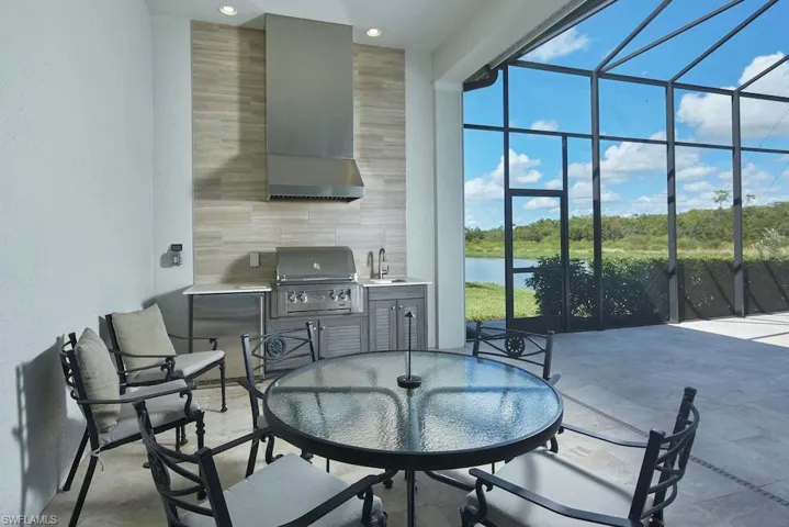 View of patio / terrace with area for grilling, sink, glass enclosure, a water view, and exterior kitchen