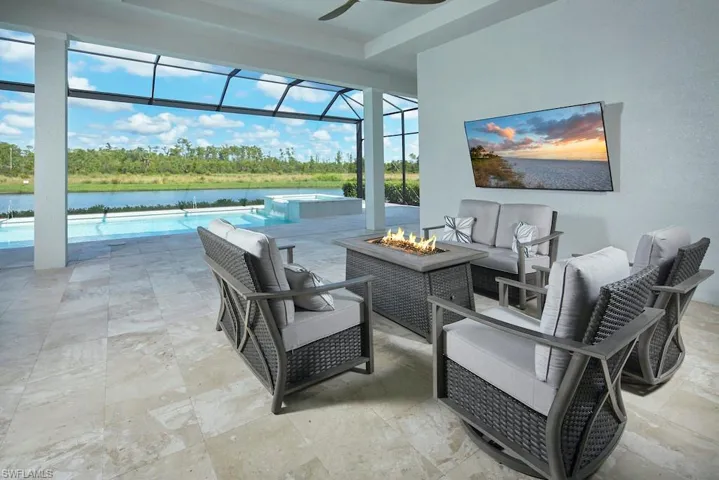 View of patio with a lanai, a water view, and an outdoor living space with a fire pit