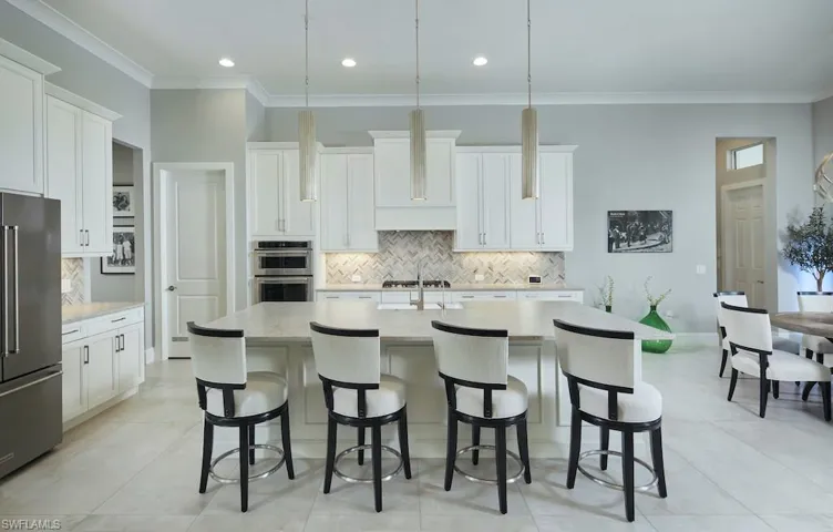 Kitchen featuring light tile patterned flooring, an island with sink, white cabinets, appliances with stainless steel finishes, and decorative light fixtures