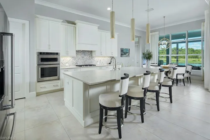 Kitchen with light stone counters, white cabinets, pendant lighting, a kitchen island with sink, and gas stovetop