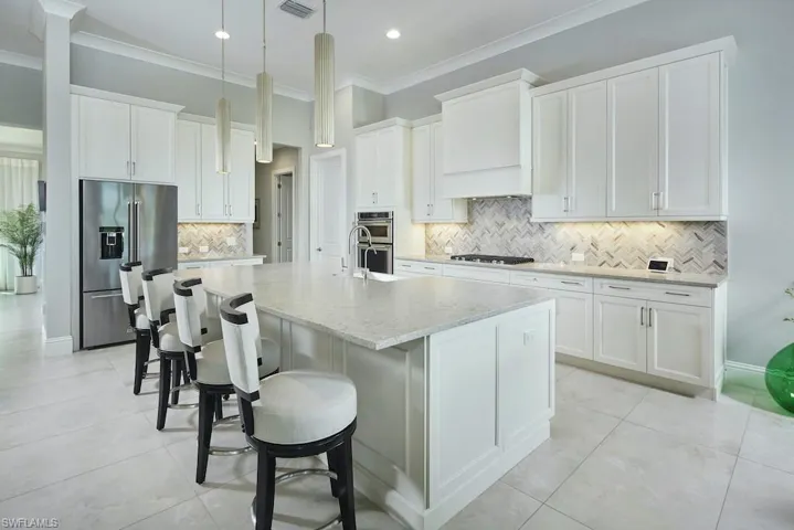 Kitchen with an island with sink, stainless steel appliances, white cabinets, and backsplash