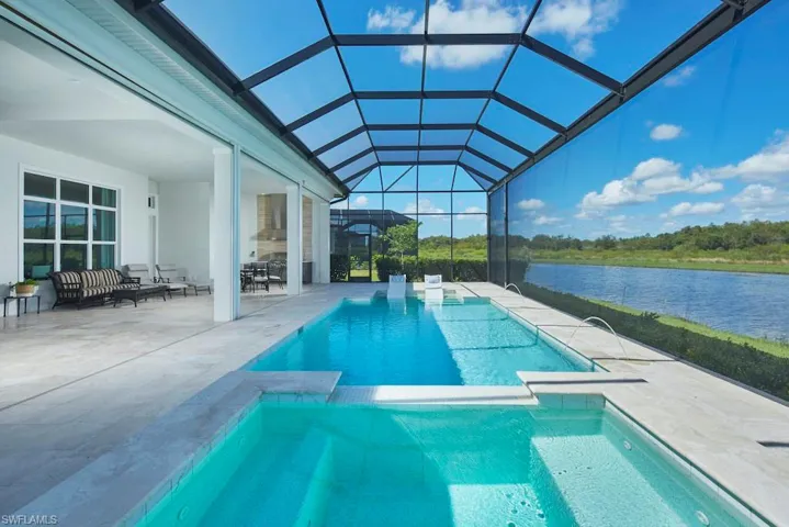 View of swimming pool featuring glass enclosure, a water view, and a patio area
