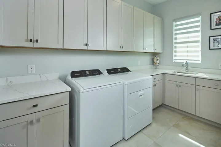 Laundry area featuring cabinets, independent washer and dryer, light tile patterned flooring, and sink