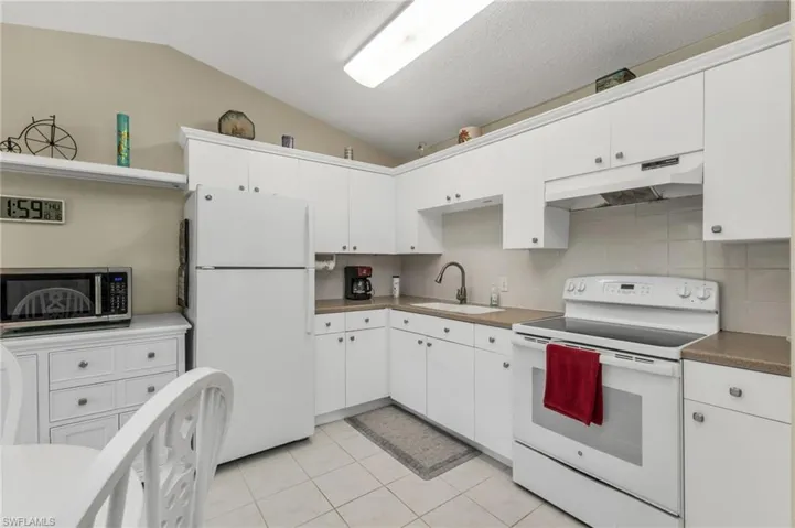 Kitchen featuring white appliances, white cabinetry, under cabinet range hood, lofted ceiling, and decorative backsplash