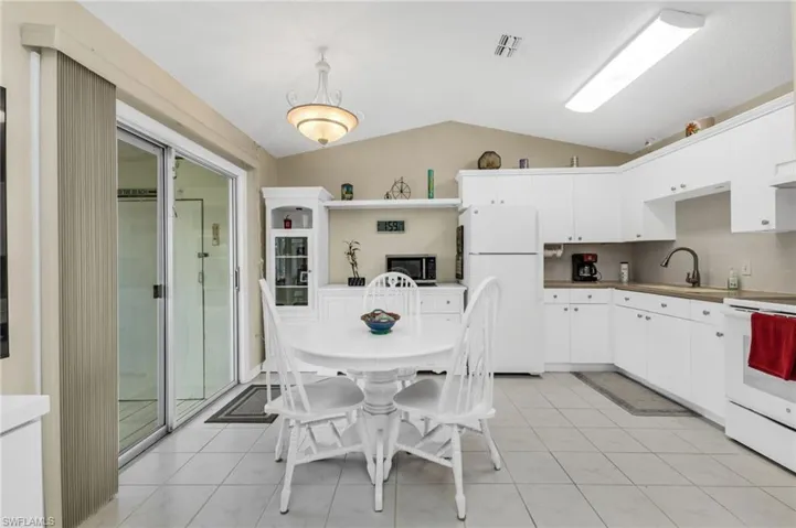 Kitchen with white cabinetry, white appliances, vaulted ceiling, light tile patterned floors, and tasteful backsplash