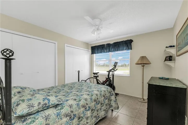 Bedroom with multiple closets, light tile patterned flooring, ceiling fan, and a textured ceiling