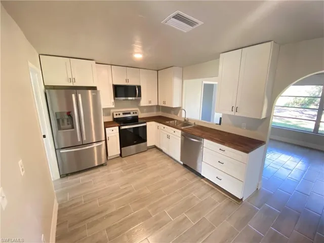 Kitchen featuring stainless steel appliances, butcher block countertops, wood tiled floors, and white cabinets