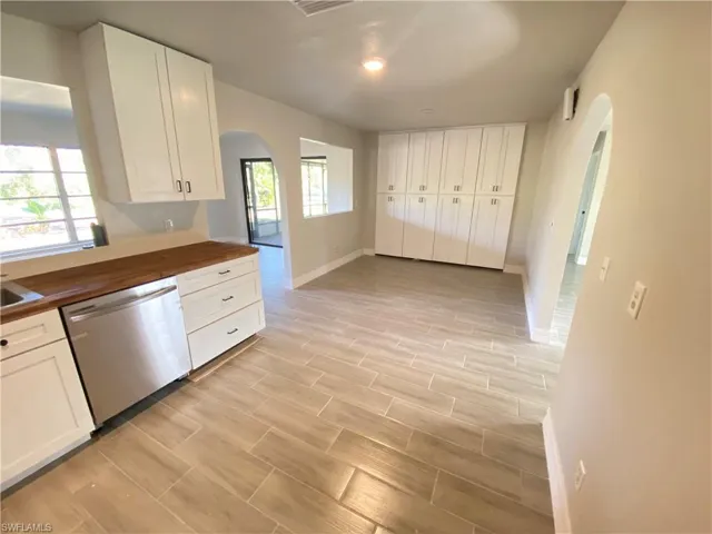 Kitchen with wood counters, arched walkways, wood tiled floors, dishwasher, and white cabinets
