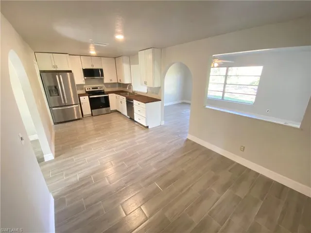 Kitchen with arched walkways, stainless steel appliances, white cabinetry, wood tiled floors, and dark countertops