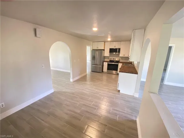 Kitchen featuring arched walkways, dark countertops, wood finish floors, stainless steel appliances, and white cabinets