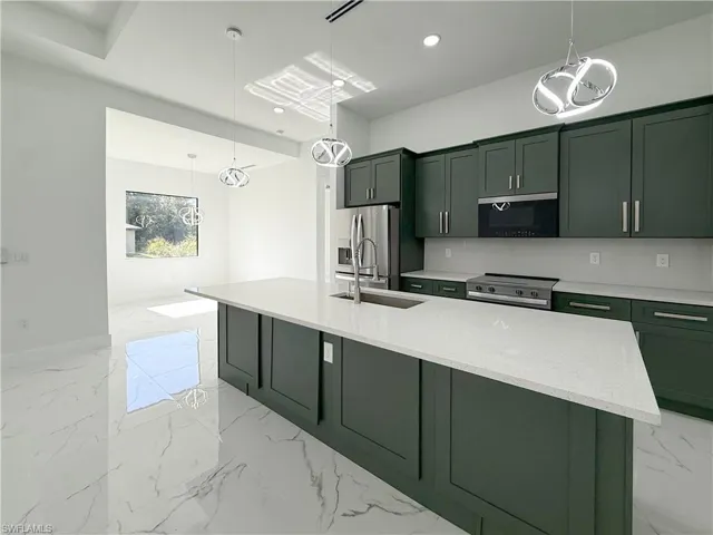 Kitchen with green cabinetry, a chandelier, light marble finish floors, light stone counters, and stainless steel appliances