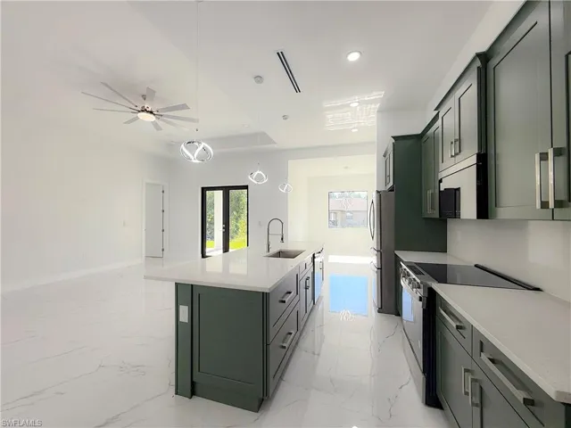 Kitchen with stainless steel appliances, an island with sink, hanging light fixtures, green cabinetry, and light marble finish floors