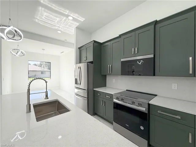 Kitchen featuring appliances with stainless steel finishes, hanging light fixtures, light stone countertops, green cabinetry, and recessed lighting