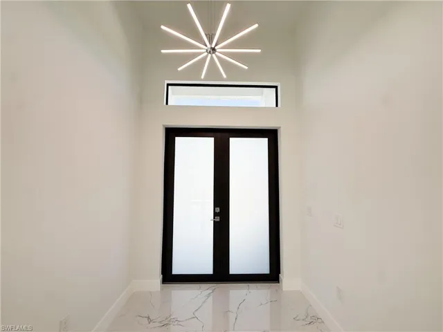 Entryway with light marble finish flooring, a chandelier, a towering ceiling, and french doors