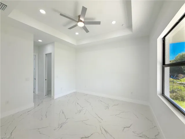 Spare room with a raised ceiling, light marble finish floors, recessed lighting, and ceiling fan