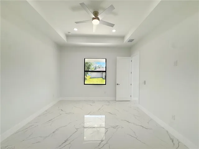 Spare room featuring light marble finish flooring, a raised ceiling, recessed lighting, and ceiling fan