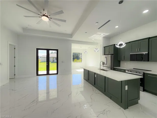 Kitchen with decorative light fixtures, stainless steel appliances, a center island with sink, light marble finish flooring, and french doors