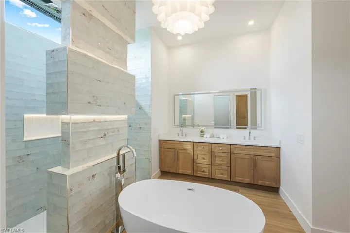 Full bath featuring double vanity, a soaking tub, a chandelier, wood finished floors, and a tile shower