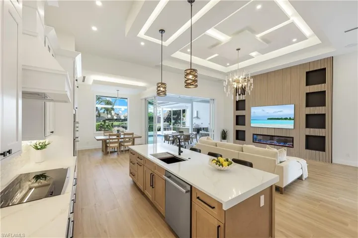 Kitchen with stainless steel dishwasher, black electric cooktop, custom exhaust hood, light wood finished floors, and a large island with sink