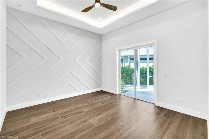 Empty room featuring ceiling fan, wood finished floors, baseboards, and a raised ceiling