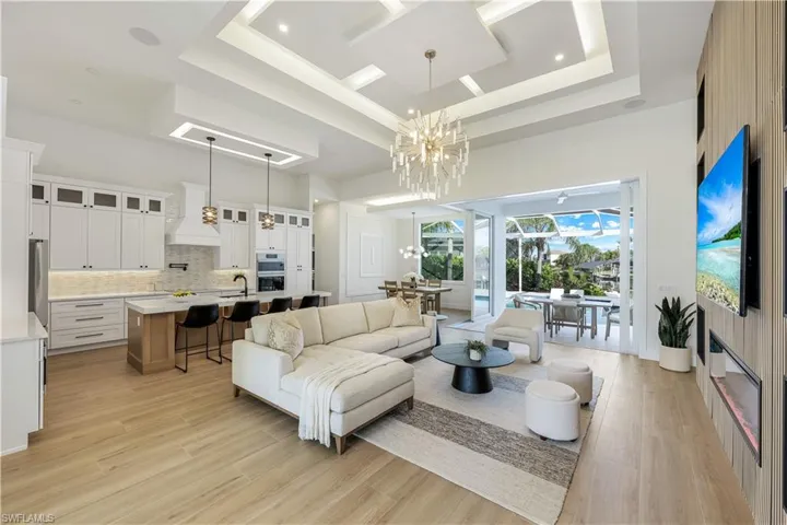 Living room with a towering ceiling, a chandelier, a raised ceiling, and light wood-style floors