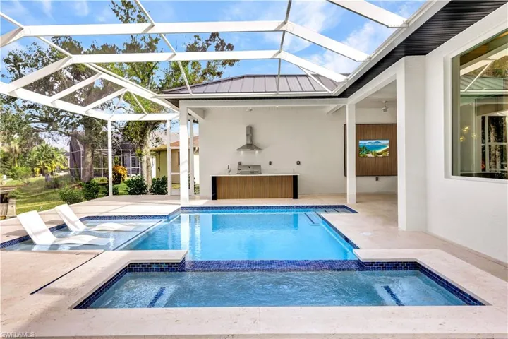 View of swimming pool featuring a pool with connected hot tub, a lanai, exterior kitchen, and a patio