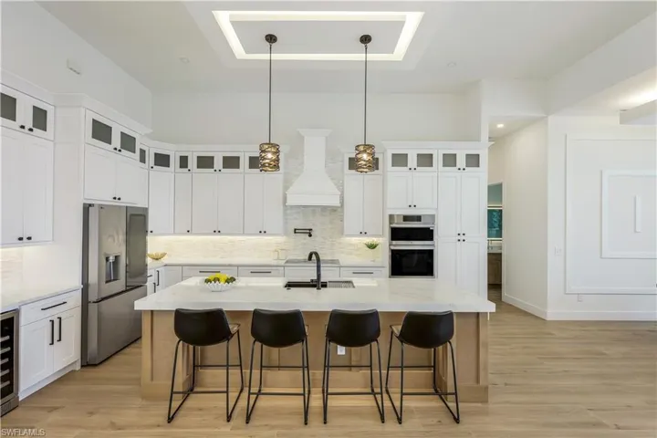 Kitchen with appliances with stainless steel finishes, premium range hood, decorative backsplash, wine cooler, and light wood-type flooring