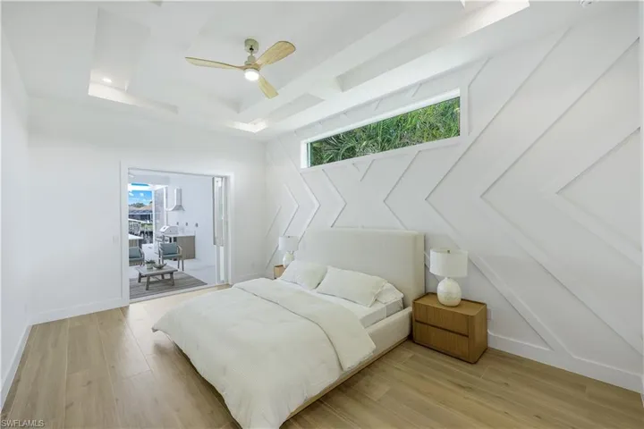 Bedroom with multiple windows, access to exterior, a tray ceiling, and light wood-style floors
