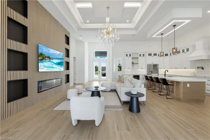 Living area featuring a towering ceiling, a glass covered fireplace, a chandelier, light wood-style floors, and wine cooler