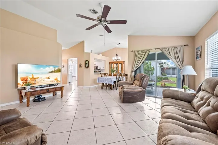 Living room with light tile patterned floors, ceiling fan with notable chandelier, lofted ceiling, and plenty of natural light