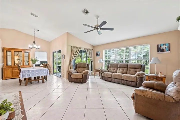 Tiled living room with lofted ceiling and ceiling fan with notable chandelier
