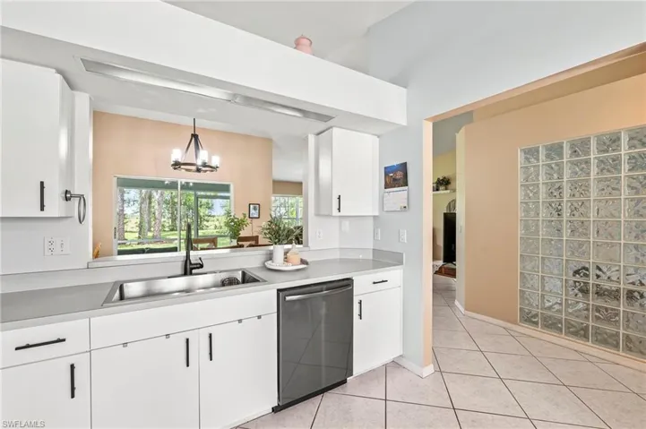 Kitchen featuring stainless steel dishwasher, white cabinetry, hanging light fixtures, sink, and light tile patterned floors