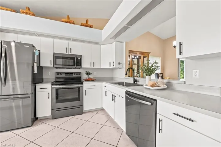 Kitchen with sink, stainless steel appliances, light tile patterned floors, and white cabinets
